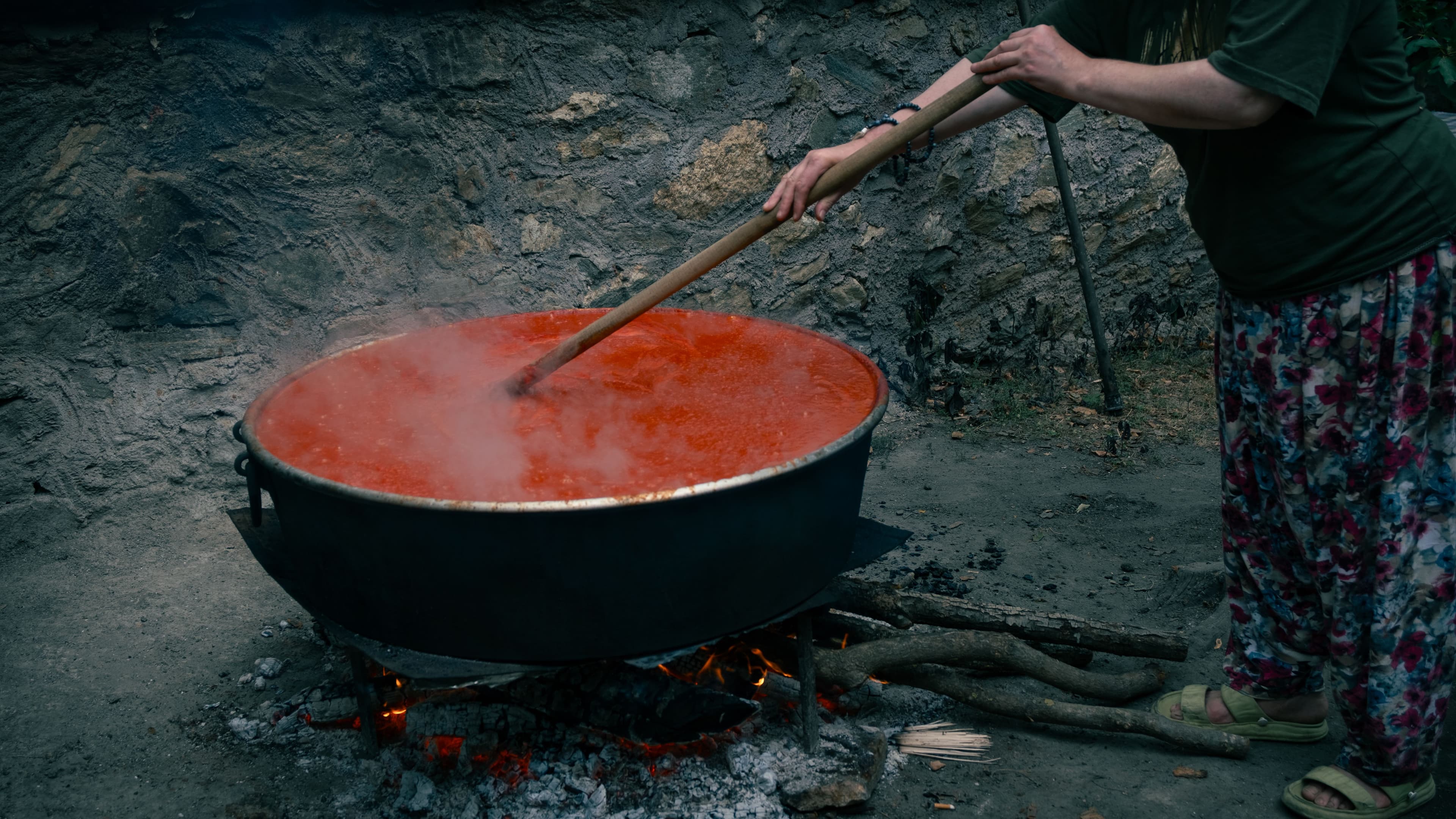Kooperatif üyesi bir kadın, odun ateşinde bakır kazanda salça kaynatıyor